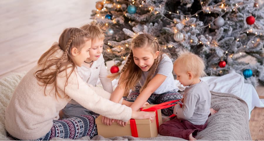 Siblings opening a present in the living room near a Christmas tree.